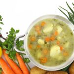 Fresh vegetable soup in a pot with mixed vegetables around it