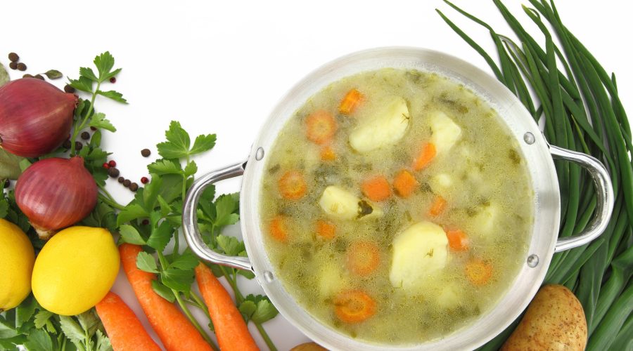 Fresh vegetable soup in a pot with mixed vegetables around it